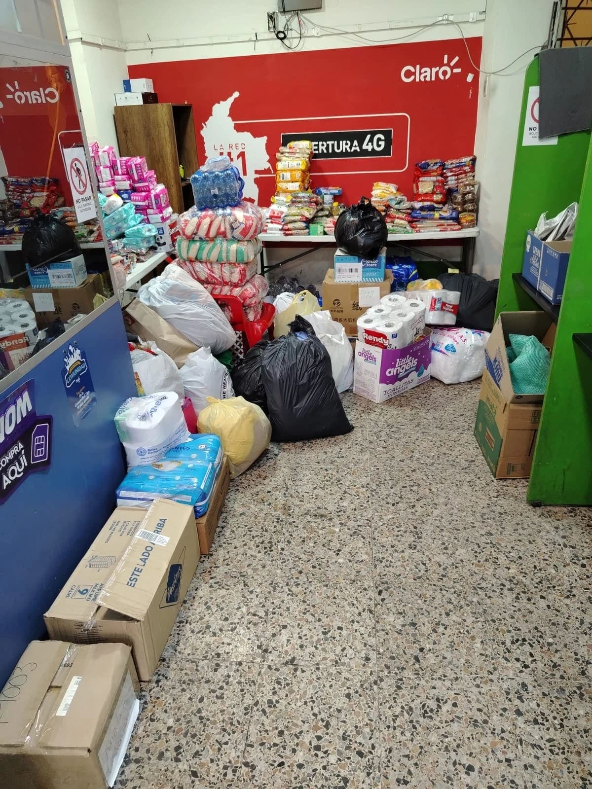 Centro de acopio con el piso y las mesas cubiertos de bolsas, cajas, pañales, papel higiénico y paquetes de arroz y pastas