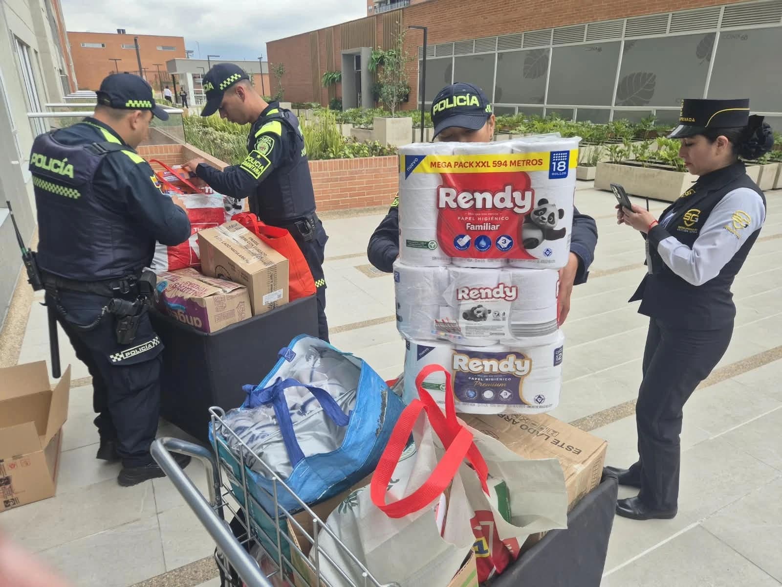 Patrulleros de la Policía Comunitaria y personal de seguridad cargando en un carro los paquetes de papel higiénico, cajas y bolsas donadas, en el acceso de Iconik 68